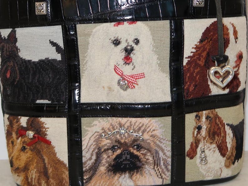 May include: Black leather tote bag with a tapestry design featuring various dog breeds. The bag has a black leather handle and trim, with silver-tone hardware. The tapestry panels showcase detailed portraits of different dogs.