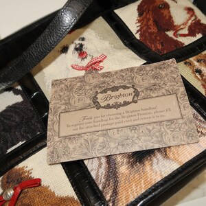 May include: A black leather handbag with a patchwork design featuring embroidered dog portraits. The bag has a top handle and a decorative card that reads "Brighton". The card includes text about registering the handbag.
