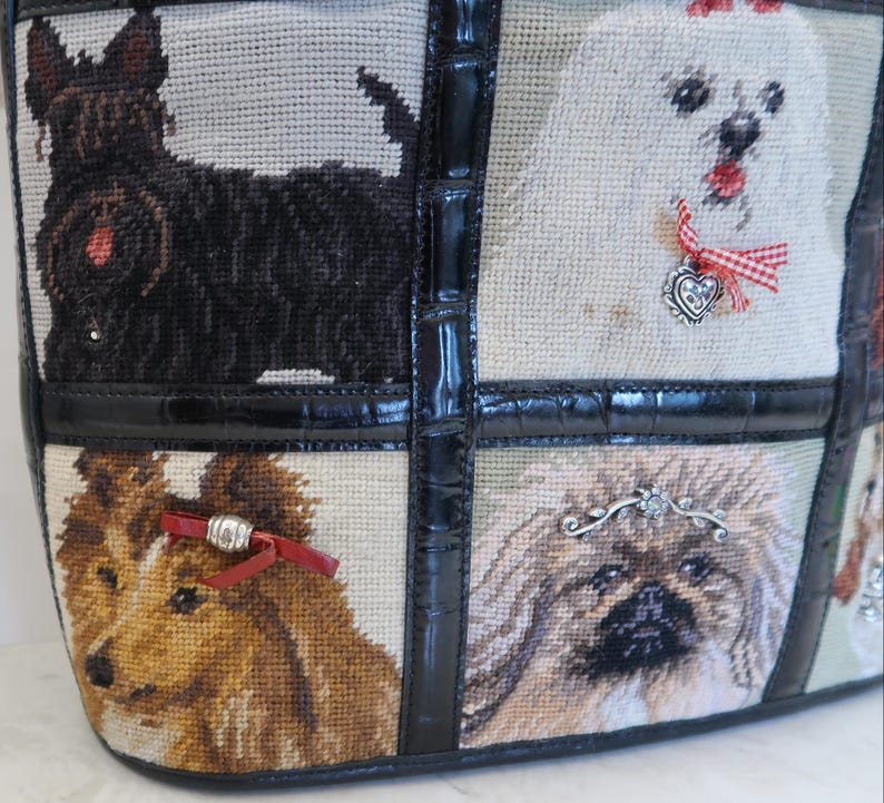 May include: Tote bag featuring a tapestry design with various dog breeds. The bag has a black leather trim and handle. The tapestry includes a black Scottish Terrier, a white dog with a red bow, a brown and white dog, and a fluffy dog.