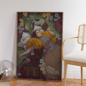 May include: A framed art print featuring a woman reclining in a field of flowers, reading a book. The artwork has a vintage aesthetic with a muted color palette. The text "POOR THINGS" is visible at the bottom of the print.
