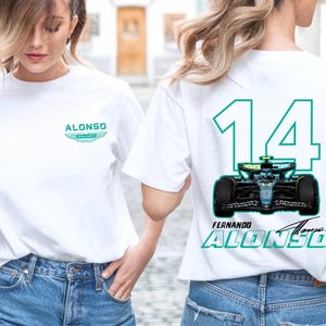 Könnte beinhalten: Weißes T-Shirt mit einem teal- und weißen "ALONSO"-Logo und Flügeldesign auf der Vorderseite. Auf der Rückseite befinden sich die Nummer "14" in Teal, eine Rennwagengrafik und "FERNANDO ALONSO" in Teal.