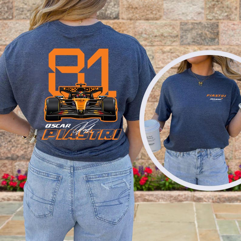 May include: A navy blue t-shirt featuring a Formula 1 race car design with the number 81 in orange. The shirt also displays the name "Oscar Piastri" and the McLaren logo. The design is on the back of the shirt.