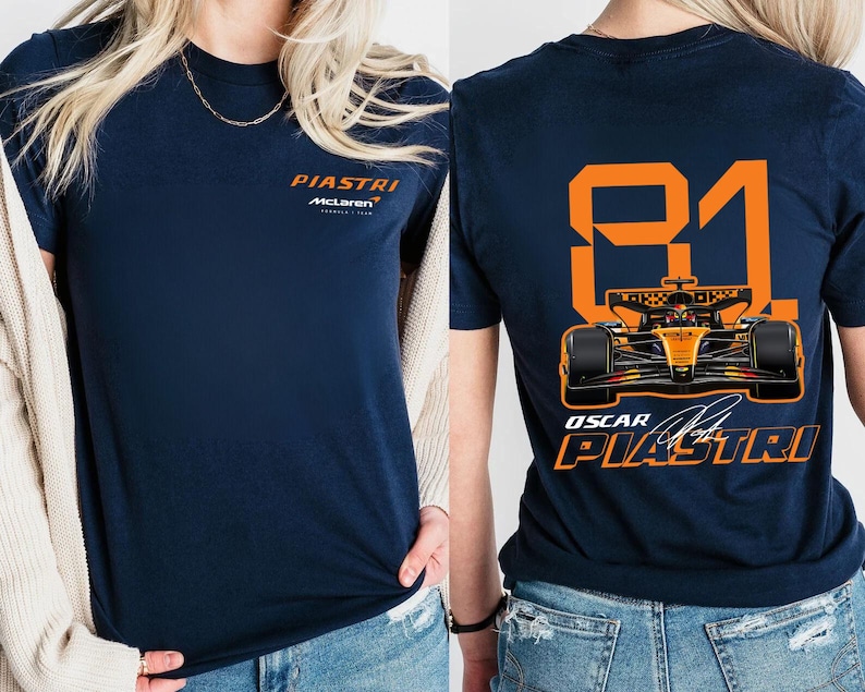 May include: Navy blue t-shirt featuring the name "PIASTRI" and "McLaren" in orange on the front. The back displays the number "81" and a Formula 1 car graphic, along with "OSCAR PIASTRI" in orange.