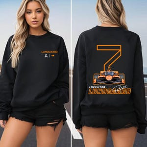 May include: Black sweatshirt with orange text and a graphic of a race car on the back. The text on the back reads "Christian Lundgaard" and the number "7". The text on the front reads "LUNDGAARD A1".