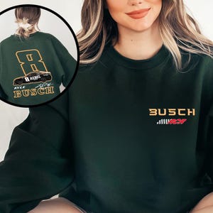 Puede incluir: Una sudadera verde oscuro con un dise&ntilde;o de bandera a cuadros blanco y rojo y el texto "Busch" en amarillo. La parte posterior de la sudadera tiene un gran n&uacute;mero "8" en amarillo con un coche negro y el texto "Kyle Busch" en blanco.