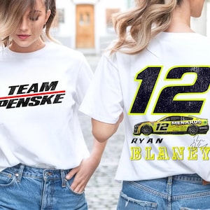 May include: Two white t-shirts with a racing theme. One shirt has the text "TEAM PENSKE" in black with a red line. The other shirt has the number "12" in black with a yellow outline, the text "MENARDS" in black, and the text "RYAN BLANEY" in yellow.