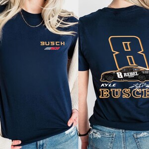 Puede incluir: Una camiseta azul marino con un logotipo "Busch" blanco y rojo y un peque&ntilde;o gr&aacute;fico de coche de carreras. La parte posterior de la camiseta presenta un gran n&uacute;mero naranja "8" con las palabras "Kyle Busch" y "Rebel" en el coche.