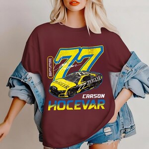 May include: Maroon t-shirt with a yellow and blue graphic of a race car, number 77, and the name "Zeigler". The text "Carson Hocevar" is below the car. The shirt has a distressed, vintage appearance.