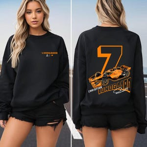 May include: Black sweatshirt with the name "Lundgaard" and the letter "A" printed in orange on the front. The back features a large orange number "7" and a race car graphic with the name "Christian Lundgaard".