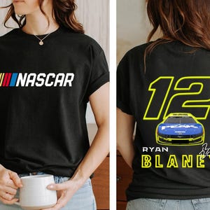 May include: Black t-shirt with a white "NASCAR" logo on the front and a yellow number "12" with a blue race car and "RYAN BLANEY" text on the back.