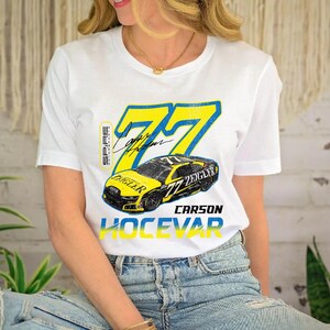 May include: White t-shirt with a yellow and blue graphic of a race car, the number 77, and the name "Carson Hocevar". The shirt also features the name "Ziegler" and a signature.