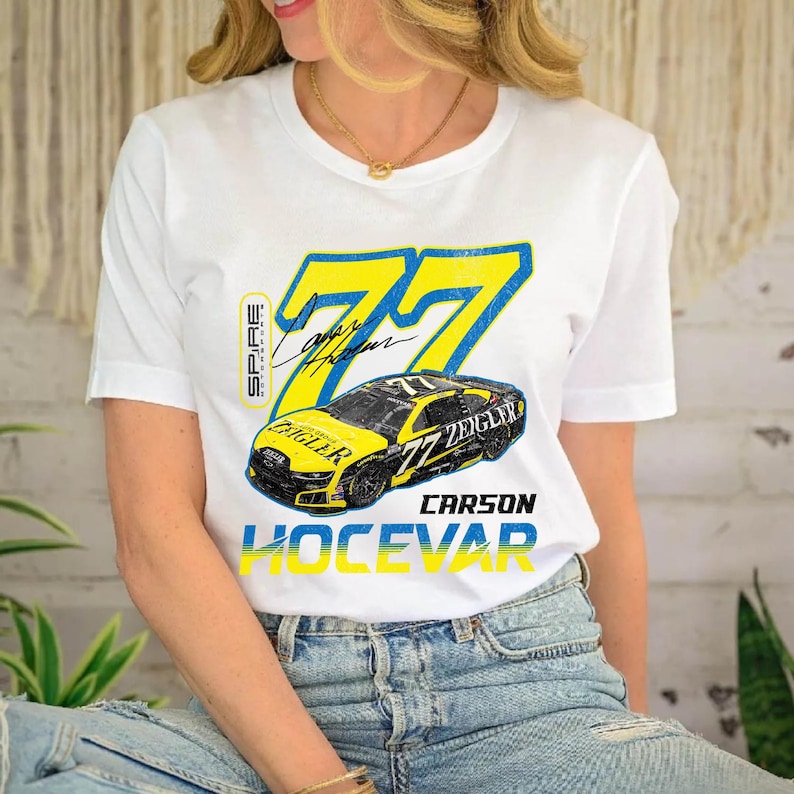 May include: White t-shirt with a yellow and blue graphic of a race car, the number 77, and the name "Carson Hocevar". The shirt also features the name "Ziegler" and a signature.
