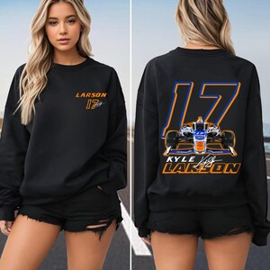 K&ouml;nnte beinhalten: Schwarzer Pullover mit einer gro&szlig;en orangen und blauen Nummer 17 auf der R&uuml;ckseite. Die Nummer umschlie&szlig;t ein kleines Bild eines Rennwagens. Der Text "KYLE LARSON" befindet sich unter der Nummer. Die Vorderseite des Pullovers tr&auml;gt den Text "LARSON 17" in Orange und Blau.