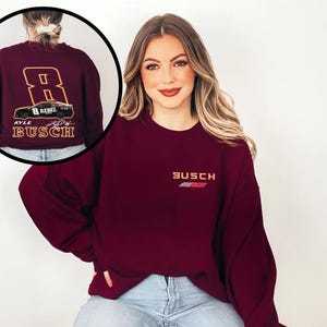 Puede incluir: Sudadera color burdeos con un dise&ntilde;o de franja de carreras blanca y roja y el texto "Busch" en la parte delantera. La parte posterior de la sudadera presenta un coche de carreras con el n&uacute;mero 8 y el texto "Kyle Busch".