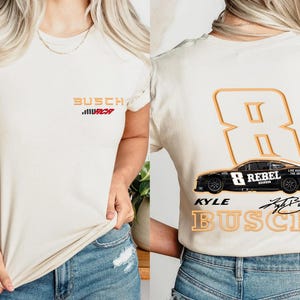 Puede incluir: Dos camisetas blancas con un dise&ntilde;o negro y naranja. La parte delantera de la camiseta tiene el texto "Busch" y "URCR" en rojo. La parte trasera de la camiseta tiene un gran n&uacute;mero naranja "8" con el texto "Kyle Busch" y "Rebel" en un coche negro.