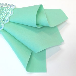 May include: A folded piece of light green felt fabric. The fabric is smooth and has a soft texture.