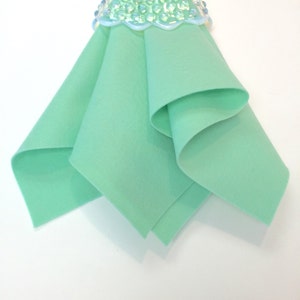 May include: A folded piece of light green felt fabric. The felt is smooth and has a soft texture.