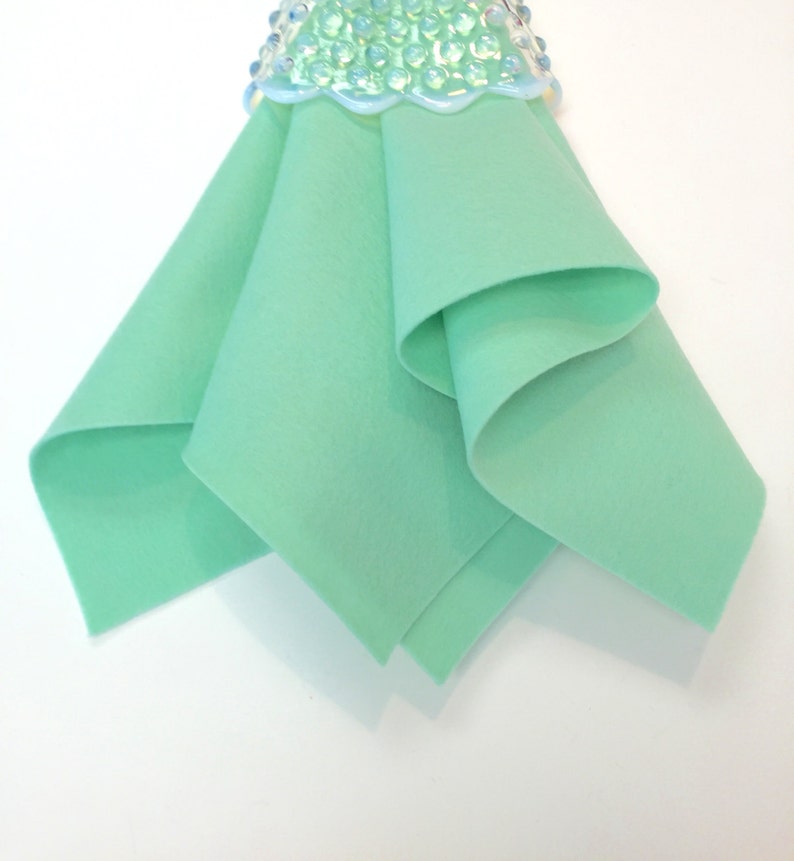 May include: A folded piece of light green felt fabric. The felt is smooth and has a soft texture.