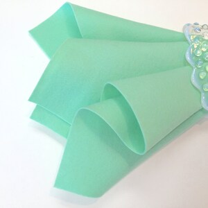 May include: A folded piece of light green felt fabric. The fabric is soft and smooth, and it is ideal for crafting projects.