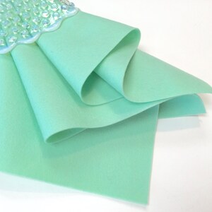 May include: A folded piece of light green felt fabric. The felt is smooth and has a soft texture.
