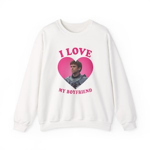 May include: White sweatshirt with the text "I LOVE MY BOYFRIEND" in pink. The design features a pink heart with a photo of a man inside. The sweatshirt has long sleeves and a crew neck.