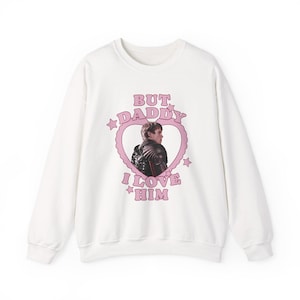 May include: White sweatshirt with a pink heart-shaped graphic. The graphic features a photo of a person and the text "BUT DADDY I LOVE HIM" in pink. The sweatshirt has a crew neck and long sleeves.