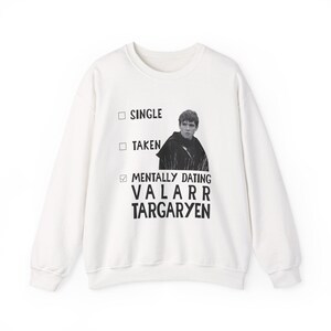 以下が含まれることがあります： 「SINGLE」、「TAKEN」、そして「MENTALLY DATING VALARR TARGARYEN」の文字が入った白いスウェットシャツ。スウェットシャツには、人物の白黒画像がプリントされています。クルーネックのスタイルのスウェットシャツです。