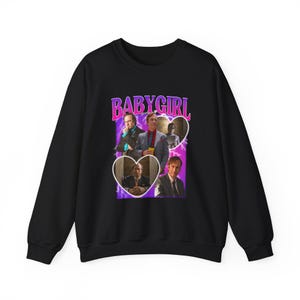 Peut inclure: Sweat-shirt noir avec un motif graphique. Le motif présente le texte "BABY GIRL" en rose et violet, ainsi que des images d'un homme dans des cadres en forme de cœur. Style décontracté.