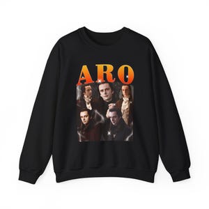 May include: Black sweatshirt featuring a collage of images and the word "ARO" in orange and yellow. The images appear to be of a person in various poses. The sweatshirt is a crew neck style.