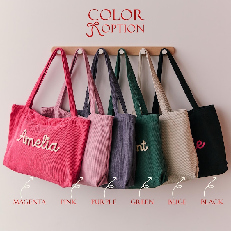 May include: Six corduroy tote bags hanging on a wooden rack, labelled COLOR OPTION. The bags are magenta, pink, purple, green, beige, and black. The magenta bag features the name Amelia in white script, while other bags show partial text.