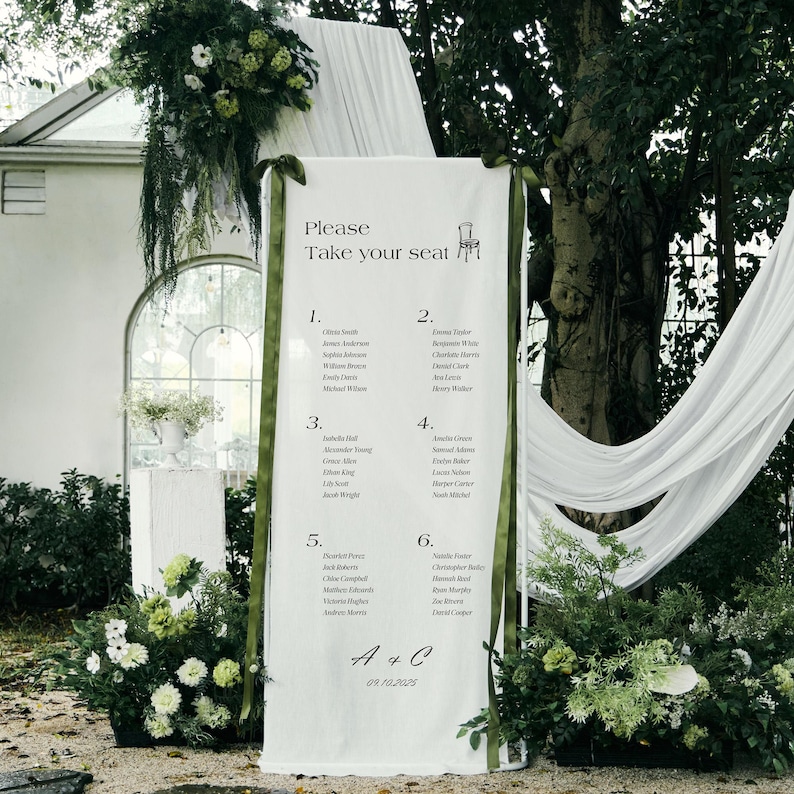 May include: A white wedding seating chart with green ribbon accents and floral decorations. The text reads "Please Take your seat" and lists names under numbers 1-6. The date "09.10.2025" is also displayed. The setting is outdoors.