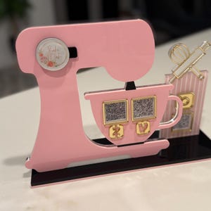 May include: Pink acrylic stand-up decoration in the shape of a mixer, with a cup and a rolling pin and whisk. The mixer has a floral design on the side and the text "Bake with Nat". The cup has two QR codes.