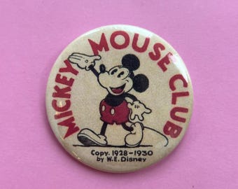 May include: A vintage Mickey Mouse Club button featuring Mickey Mouse in a classic pose. The button has a beige background with red text that reads "Mickey Mouse Club." The copyright information "Copy. 1928-1930 by W.E. Disney" is also visible.