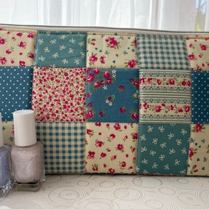 May include: A patchwork fabric zippered pouch with a blue, white and pink floral pattern. Three bottles of light purple nail polish are in front of the pouch.