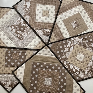 May include: Set of six brown and white quilted placemats with a geometric pattern. The placemats have a brown border and are made of fabric with a variety of textures.