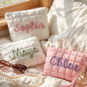 Puede incluir: Tres estuches acolchados con cremallera en blanco y rosa claro. Dos estuches blancos llevan los nombres Sophia en rosa y Maya en verde, mientras que el estuche rosa lleva el nombre Chloe en morado. Incluye un collar de perlas, gafas y perfume.