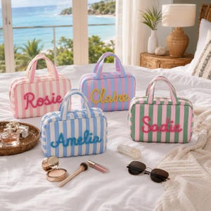 May include: Four rectangular striped cosmetic bags with top handles and embroidered names. One bag is pink and white with Rosie, one is blue and white with Amelia, one is blue and pink with Claire, and one is green and white with Sadie.