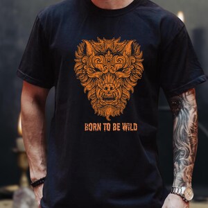May include: Black t-shirt with an orange wolf head design and the text "BORN TO BE WILD". The illustration is detailed and ornate. The t-shirt has a crew neck and short sleeves.