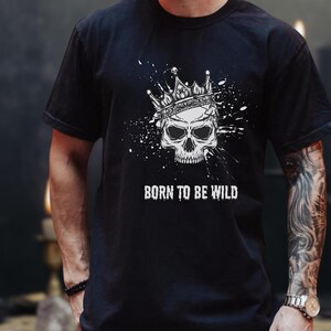 May include: Black t-shirt with a white skull and crown graphic, and paint splatter effect. The words "BORN TO BE WILD" are printed beneath the skull. The shirt has a crew neck and short sleeves.