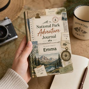 Puede incluir: Un diario de aventuras del Parque Nacional de estilo vintage con una escena de montaña y lago. El diario presenta el texto "National Park Adventure Journal" y "Emma" en la portada, junto con una brújula y la frase "Adventure Awaits."