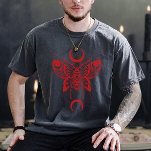 Peut inclure: T-shirt gris foncé avec un motif de papillon de nuit rouge et des détails de croissant de lune. Le papillon de nuit présente des motifs d'ailes détaillés. Le t-shirt est de style col rond et à manches courtes.