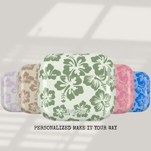 May include: Five different colored Airpod cases with a floral design. The cases are in shades of purple, brown, green, pink, and blue. The text "Katie Royce" is printed on the green case. The text "Personalized Make It Your Way" is printed below the cases.