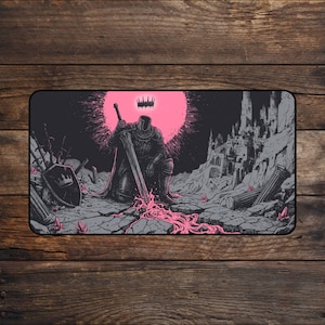 May include: A rectangular desk mat featuring a dark illustration of a headless knight in armour kneeling and holding a large sword. A bright pink sun sits behind the figure, with a ruined castle, broken pillars, and pink liquid on the ground.