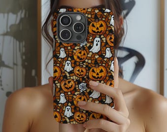 May include: A Halloween-themed phone case featuring a repeating pattern of jack-o'-lanterns, white ghosts, and spiderwebs on a mosaic-style background. The case has a black camera module and is held in front of a person.