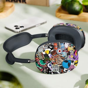 Puede incluir: Auriculares negros y grises con un dise&ntilde;o de calcoman&iacute;as coloridas. Las calcoman&iacute;as presentan una variedad de im&aacute;genes, incluyendo un pato de goma amarillo, un extraterrestre de dibujos animados y el texto "Gamers Never Sleep".