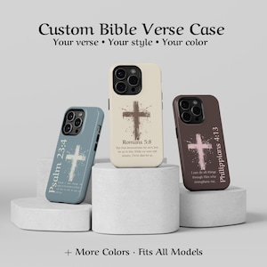 May include: Three phone cases with Bible verses and cross designs. One case is light blue with "Psalm 23:4", another is beige with "Romans 5:8", and the third is brown with "Philippians 4:13". The cases are displayed on white pedestals.