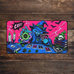 Puede incluir: Un tapete de juego rectangular que muestra a un gato mago azul con sombrero puntiagudo lanzando un hechizo con un dado de veinte caras verde brillante. El fondo es rosa intenso con rayos, murciélagos, velas, cartas de tarot y libros.