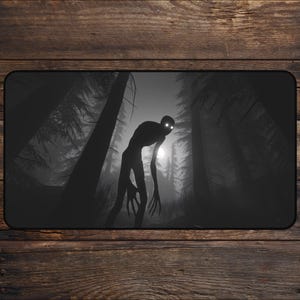 May include: Black and white mousepad featuring a silhouetted creature with glowing eyes in a dark forest. The design evokes a sense of mystery and horror, with tall trees and a bright light in the background.