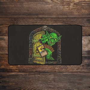 May include: A rectangular black playmat featuring a green goblin peering through a stone archway door. The goblin has sharp teeth and long fingers, holding a hand of playing cards, with one card prominently displayed in the foreground.