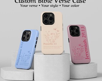 Puede incluir: Tres fundas de teléfono personalizadas en azul claro, beige y rosa, cada una con un versículo bíblico y un diseño floral. Las fundas se exhiben sobre pedestales blancos. El texto en las fundas incluye "Filipenses 4:13", "Proverbios 3:5" y "Jeremías 29:13".